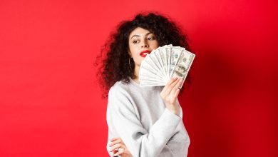 beautiful rich woman looking sensual aside waving at herself with dollar bills fan standing seductive on red background
