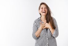 ha ha so amusing portrait of charming carefree middle aged woman in striped blouse holding hands on chest touched and pleased laughing out loud amazed and entertained standing over white wall