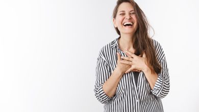 ha ha so amusing portrait of charming carefree middle aged woman in striped blouse holding hands on chest touched and pleased laughing out loud amazed and entertained standing over white wall